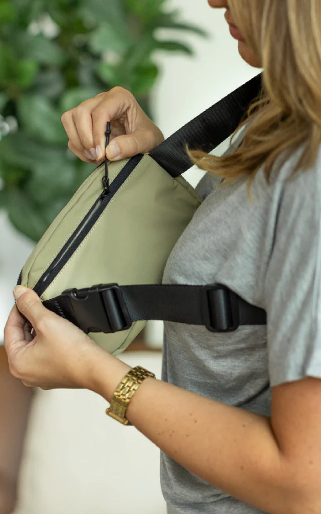 Woman showing the zipper pocket on the back of a bum bag. 